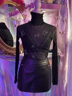 Svart y2k mesh topp med paljetter - Säljer en svart y2k mesh med transparent material och tryckt logga samt bokstäver i strassdetaljer. Toppen har lång ärm och tight passform, perfekt för att styla lager på lager eller med coola accessoarer.