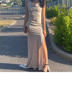 Champagnefärgad långklänning med slits - Säljer en elegant långklänning i champagnefärg med slits på sidan. Klänningen har en mjuk, glansig yta och smala axelband.🩷Materialet känns som satin eller silke och modellen är figurnära med ett snyggt fall. Perfekt för bal eller fest.💞 säljer då den inte kommer till användning längre. Klänningen är mycket bra i skick💕💕 sitter som en Xs-S