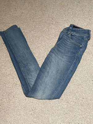 Blå jeans från Tiger of Sweden - Säljer ett par klassiska blå jeans från Tiger of Sweden. Modellen är skinny fit med normal midja och raka ben. Jeansen har fem fickor, snygga kontrastsömmar och är tillverkade i mjukt denimtyg. Perfekta till sneakers eller boots.