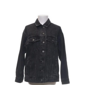 Svart jeansjacka från Bershka - Säljer en svart jeansjacka från Bershka med klassisk krage, bröstfickor med lock och knappar framtill. Jackan har en rak passform och långa ärmar.