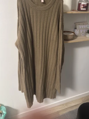 Beige ribbad stickad tröja - Lång, oversized stickad tröja i beige med ribbad struktur. Tröjan har rund halsringning och långa ärmar, perfekt för lager på lager under kyliga dagar. Enkel och stilren design som passar till det mesta.