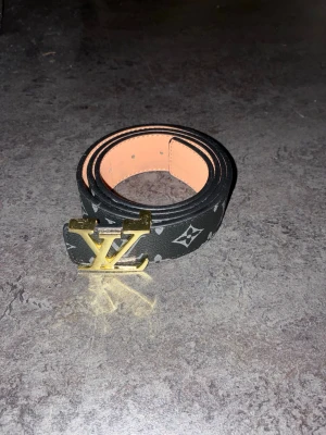 Louis Vuitton bälte - Säljer ett svart bälte från Louis Vuitton med klassiskt monogrammönster och stor guldfärgad LV-spänne. Bältet har en lyxig känsla och är tillverkat i skinn. Perfekt accessoar för att lyfta vilken outfit som helst.