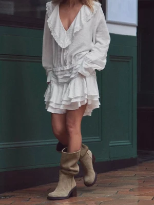 Vit volangklänning med spetsdetalj - Supersöt vit kortklänning med v-ringning och bred volangkrage dekorerad med spets. Klänningen har långa ärmar, markerad midja och flera lager volanger i kjolen för extra flow. Perfekt för dig som vill ha en romantisk och trendig look.