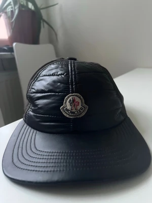 Svart Moncler keps - Äkta moncler keps jätte unik och snygg säljer till bra pris den behöver bara en liten tvätt. Annars bra skick säljer den till bra och snabbt pris.