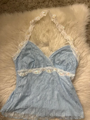 Ljusblå spetslinnetopp med paljettdetaljer - Supersöt ljusblå topp i spets med vita spetskanter och små paljetter längs halsringningen och under bysten. Toppen har en feminin v-ringning och tunna axelband som ger en romantisk vibe. Perfekt för sommardagar eller när du vill känna dig extra söt. Också köpt på Vinted står inget märke 🤷🏼‍♀️