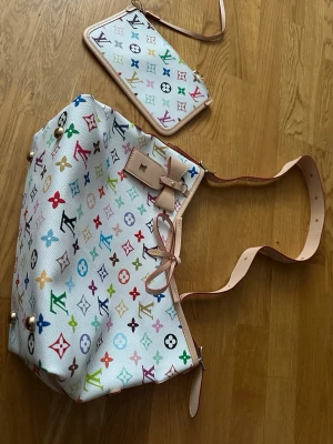 Murakami x Louis Vuitton Carryall - Säljer en Louis Vuitton x Murakami axelväska med vitt konstläder och färgglatt monogrammönster. Väskan har ljusa läderdetaljer, väskan har en matchande liten clutch. Insidan är beige med innerfack och dragkedja. Den är helt ny oanvänd, jag fick den som present men vet tyvärr inte om den är äkta men den är jätte fin
