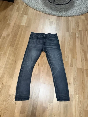 Slim fit jeans från H&M, grå - Slim fit jeans från H&M i en mörkgrå tvätt med snygga slitningar och klassisk femficksdesign. Jeansen har raka ben och normal midja, tillverkade i bomullsmix för en bekväm känsla. Perfekta för dig som gillar en stilren och modern look.