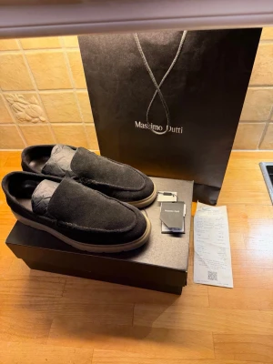 Svarta mockaloafers från Massimo Dutti - Snygga loafers i svart mocka från Massimo Dutti med beige, räfflad sula. Skorna har en stilren design med rund tå och diskreta sömmar längs ovandelen. Perfekta för dig som vill ha en clean och modern look till vardagsoutfiten.