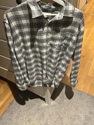 Rutig skjorta från NN07 i bomull - Säljer en stilren rutig overshirt från NN07 i svart och vitt. Den har klassisk krage, bröstficka och knäppning framtill. Tillverkad i mjuk bomull och har långa ärmar med knapp vid manschetten. Perfekt för dig som gillar avslappnad men snygg stil.