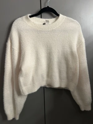 Vit fluffig stickad tröja S - Mysig vit stickad tröja i fluffigt material. Tröjan har en croppad passform, rund halsringning och långa ärmar. Perfekt för kyliga dagar och enkel att styla med jeans eller kjol.