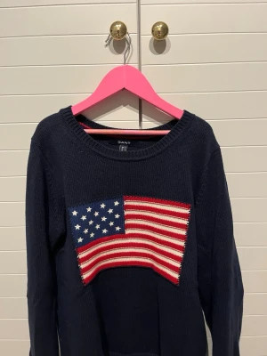 Mörkblå stickad tröja GANT S - Snygg stickad tröja från GANT i mörkblå färg med ett broderat USA-flagga-motiv framtill  Tröjan är i okej skick, använd men fortfarande fullt fin att bära 