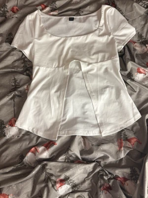 Vit topp med slits från SHEIN - Säljer en vit topp från SHEIN i storlek S med korta ärmar och rundad urringning. Toppen har en unik slitsdetalj framtill som ger en cool twist till looken. Tillverkad i ett mjukt och lätt material som känns skönt mot huden.🩷