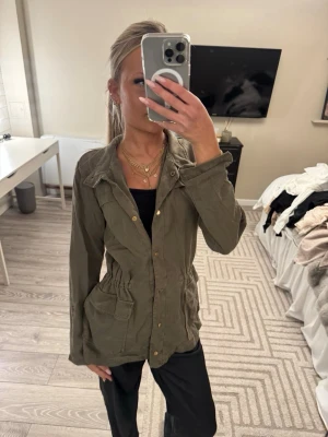 Olivgrön manchesterjacka med fickor - Snygg olivgrön jacka i manchester med stora fickor framtill och knappar hela vägen. Jackan har en markerad midja med resår och klassisk krage. Perfekt för dig som gillar en avslappnad men ändå trendig stil.