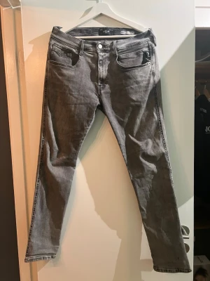 Replay Anbass Hyperflex grå jeans - Säljer ett par grå Replay Anbass Hyperflex jeans med slim fit. Jeansen har klassisk femficksdesign, silverfärgad knapp och dragkedja. Materialet är stretchigt och bekvämt, perfekt för dig som vill ha både stil och rörelsefrihet. Färgen är snyggt tvättad grå. Lite sliten!  (se sista bilden litet hål!)  storlek w33 och 30 L
