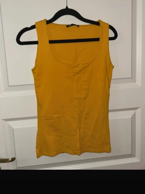 Gul linnetopp från Zara - Snygg gul linnetopp från Zara i storlek S. Toppen har breda axelband och en rundad urringning framtill. Tillverkad i mjuk bomull som känns skön mot huden. Perfekt till sommaren och enkel att matcha med jeans eller kjol.