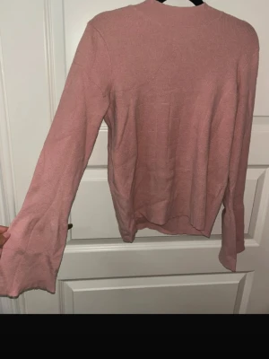 Ljusrosa stickad tröja från Pieces - Supersöt ljusrosa stickad tröja från Pieces med långärmad passform och lätt utsvängda ärmar. Perfekt till både jeans och kjol, enkel att styla och riktigt skön att ha på sig. Ribbad vid halsen för extra detalj.