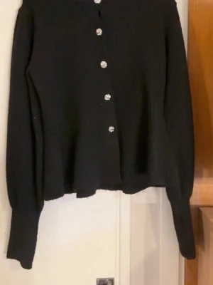 Svart kofta från PIECES med Silver knappar - Svart ribbad tröja från Pieces i strl S, med jättefina silver knappar framtill. Sitter super fint på kroppen med lite utsvängd form nertill som ger en smickrande passform. Mjuk och skön att ha på sig, funkar lika bra till vardag som till fest.  Använd fåtal gånger och i mycket fint skick, inga skador eller noppor. Perfekt till jeans, kjol eller kostymbyxor. köpt på vero moda