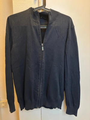 Mörkblå kofta med dragkedja - Mörkblå kofta från SIXTH SENSE MORE med hel dragkedja framtill och ribbade muddar vid hals, ärmslut och nederkant. Långärmad och i mjukt material, perfekt för lager på lager under kyligare dagar.