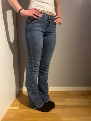 Blå bootcut jeans med mellan hög midja  - Säljer ett par klassiska blå jeans med bootcut och hög midja. Jeansen har fem fickor, dragkedja och knapp framtill. Materialet är stretchigt jeans som sitter snyggt och bekvämt. Perfekta till sneakers eller boots.