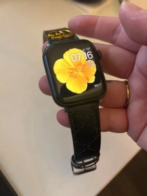 Apple Watch med Gucci-armband - Stilren Apple Watch med exklusivt svart Gucci-läderarmband. Klockan har en tydlig 44mm skärm och är i gott skick. Perfekt för dig som vill kombinera smart teknik med lyxig design. Levereras med originalarmband från Gucci. 