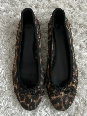 Leopardmönstrade ballerinaskor från H&M - Snygga nya ballerinaskor i storlek 37 från H&M med leopardmönster i svart och brunt. Skorna har rund tå och en liten rosett framtill 🤎