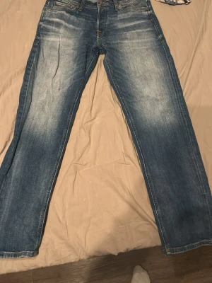 Blå jeans från Jack & Jones - Säljer ett par klassiska blå jeans från Jack & Jones med snyggt slitna detaljer och raka ben. Jeansen har fem fickor, normal passform och är tillverkade i tåligt denimtyg. Perfekta för en avslappnad och stilren look.