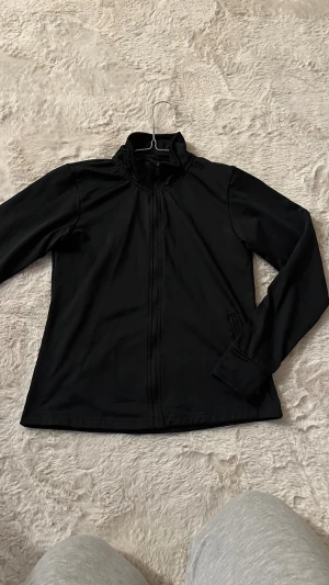 Svart vindjacka från SOC - Säljer en svart vindjacka från SOC i storlek 146/152. Jackan har hög krage, hel dragkedja framtill och två sidofickor. Perfekt för dig som vill ha en enkel och sportig jacka till vardagen. Materialet är lätt och känns smidigt. Passar XS