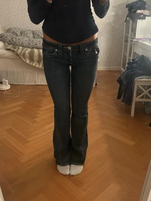 Mörkblå bootcut jeans med vita sömmar - Säljer ett par mörkblå jeans med bootcut-modell och låg midja. Jeansen har tydliga vita kontrastsömmar, klassiska fem fickor och snygga detaljer på bakfickorna. Materialet är jeans och passformen är normal med lätt utsvängda ben.