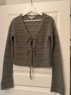 Grå stickad kofta med knyt från Amisu - Supersöt grå stickad kofta från Amisu med v-ringning och två knyt framtill. Koftan har ett fint hålmönster och långa ärmar. Perfekt att slänga över en topp för en chill look.