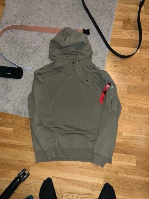 Alpha Industries hoodie / anorak – Olive green – Strl L - Säljer en Alpha Industries hoodie/anorak i olive green. Klassisk “Remove Before Flight”-tag på ärmen och diskret logga på bröstet.  Bra skick, inga hål eller större defekter och Tjock och skön kvalitet, perfekt till höst/vinter   Skickas snabbt  Hör av dig vid frågor eller bud.