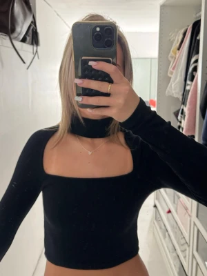 Svart croppad långärmad topp - Snygg svart croppad topp med lång ärm och fyrkantig urringning. Toppen har en hög hals som ger en cool och trendig look. Perfekt att styla med jeans eller kjol för en modern outfit.