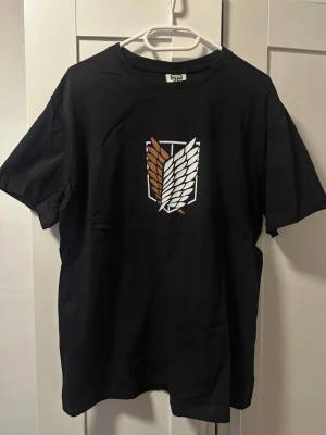 Attack on Titan t-shirt från RISE - etikett - Svart t-shirt från RISE med stort tryck av Attack on Titan och Levi Ackerman tryck på ryggen. Storlek L i unisex passform, så passar alla! Nyskick, med etikettet!
