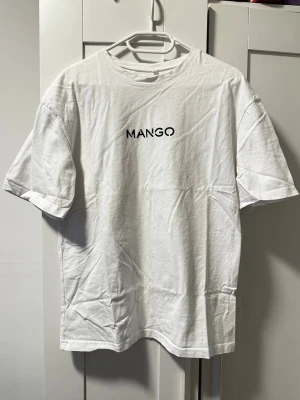 Vit t-shirt från Mango - Vit t-shirt från Mango med svart logga tryckt på bröstet. Klassisk rund hals och korta ärmar. Tillverkad i mjuk bomull som känns skön mot huden. Enkel och clean design som funkar till det mesta. Storlek S men är i lite mer oversize modell. Nyskick aldrig använd. Har legat vikt i skåpet därav lite skrunklig