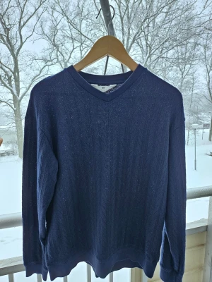 Stickad tröja  - Säljer en marinblå stickad tröja från H&M med diskret och vackert mönster. Tröjan har långa ärmar och ribbade muddar vid ärmslut och nederkant. Perfekt för kyliga dagar och enkel att matcha med jeans.
