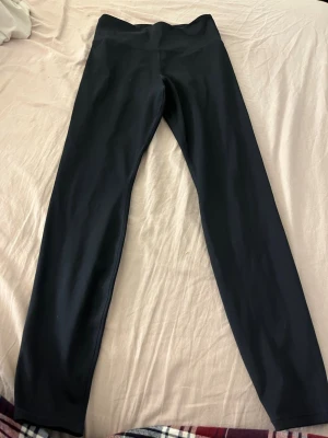 Svarta leggings från H&M Sport - Säljer ett par svarta leggings från H&M Sport i storlek S. De har hög midja och är tillverkade i ett stretchigt syntetmaterial som sitter tight och bekvämt. Perfekta för träning eller chill dagar. Klassisk och enkel design utan detaljer.