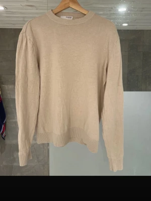Beige stickad tröja från Selected Homme - Säljer en stilren beige stickad tröja från Selected Homme. Tröjan har rund halsringning, ribbade muddar och nederkant samt lång ärm. Perfekt för lager på lager under höst och vinter. Enkel att matcha med jeans eller chinos.