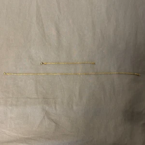  kordel kedjesmycken - Säljer ett set med två tunna kedjesmycken i guldpläterad metall. Ena är ett armband och det andra ett halsband, båda med klassisk tvinnad kedja och enkel låsanordning. Perfekt för dig som gillar minimalistisk och stilren design.