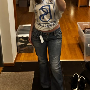 Lågmidjade bootcut jeans blå - Säljer ett par blå jeans med låg midja och bootcut passform. Köpta i Budapest och har prislappen kvar. Jeansen har klassisk femficksdesign, snygga slitningar och kontrastsömmar. Perfekta för dig som gillar en avslappnad och trendig look. Storlek: W30 L30