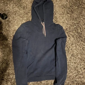 Mörkblå hoodie från Gucci med huva - Säljer en mörkblå hoodie från Gucci i storlek M. Tröjan har en klassisk huva med snörning i beige, rött och grönt, samt långa ärmar. Tillverkad i mjuk bomull och perfekt för dig som gillar stilrena designer med exklusiv känsla.