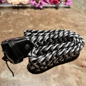 Svart och vit flätad bälte - Säljer ett snyggt flätat bälte i svart och vitt med silverfärgat spänne. Bältet är 120 cm långt inklusive allt. 