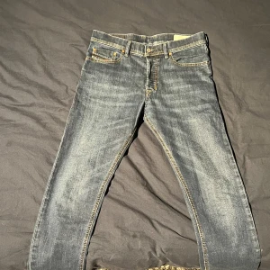 Diesel Tepphar jeans blå W29 L32 - Säljer ett par blå Diesel Tepphar jeans med snygg tvätt och kontrastsömmar. Modellen är slim carrot fit med klassiska fem fickor och guldfärgade nitar. Jeansen har stretch för extra komfort och en diskret Diesel-logga vid myntfickan.