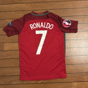 Portugal Ronaldo 7 Nike fotbollströja S - Säljer en röd Portugal fotbollströja med Ronaldo och nummer 7 på ryggen. Tröjan är från Nike med Dri-FIT material, har korta ärmar och officiella EM-patchar på båda ärmarna. Snyggt broderat landslagsemblem på bröstet och vit Nike-logga.