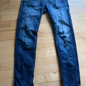 Jack & Jones blå tapered jeans - Snygga blå jeans från Jack & Jones i modellen Tapered/Mike. Jeansen har klassisk femficksdesign, normal midja och avsmalnande ben. Tillverkade i slitstarkt denimtyg som ger en cool och avslappnad look. Perfekta för dig som gillar en modern passform. W29 L32