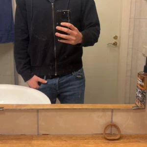 Svart hoodie från Jack & Jones - Svart hoodie från Jack & Jones med dragkedja framtill, huva med snörning och två stora fickor. Klassisk modell i mjukt material, perfekt för chill dagar. Långärmad och enkel att matcha med jeans eller joggers. Storlek XS men känns mer som S