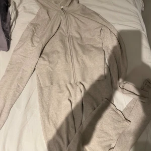 Beige mjukis sett med snörning - Beiga mjukis sett med bred ribbad midja och snörning. Byxorna är raka i modellen och tillverkade i mjukt bomullsmaterial, perfekta för chill dagar. Matchar med hoodie i samma färg för en hel look.