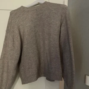 Beige stickad tröja från H&M - Mysig beige stickad tröja från H&M med rund halsringning och ribbade muddar. Tröjan har en avslappnad passform och långa ärmar, perfekt för lager-på-lager under kyliga dagar.