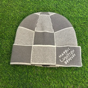 Grå rutig Łouis Vuiṯton mössa - Snygg grå och vit rutig mössa från Łouis Vuitṯon med broderad text på uppviket. Tillverkad i lyxig mix av kashmir, ull och silke. Perfekt accessoar för dig som vill sticka ut med designer vibes och mjuk känsla.
