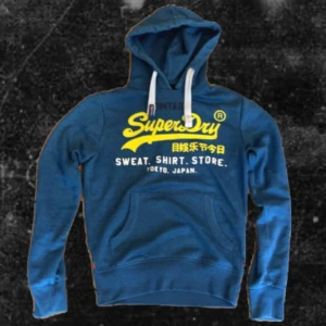 Blå Superdry Hoodie - Riktig snygg hoodie från Superdry, hoodien är i storlek XS men sitter som S/M och passar mig perfekt som är 178. Den är i fint skick och har inte större defekter förutom texten men det märks inte jättemycket vid användning.