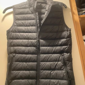 Svart  dunväst - Snygg svart dunväst från Strow i storlek XS. Västen har ett quiltat mönster med horisontella sömmar, dragkedja framtill. Utrustad med två fickor med dragkedja och en innerficka. Perfekt att slänga över en hoodie för extra värme. Figur sydd!