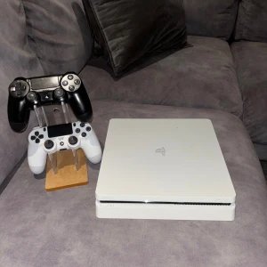 PlayStation 4 Slim Vit - Snygg vit PlayStation 4 Slim med två DualShock 4-kontroller (svart och vit). Konsolen är i gott skick med några mindre ytliga repor. Perfekt för gaming och multimedia. Alla portar synliga och i bra skick.